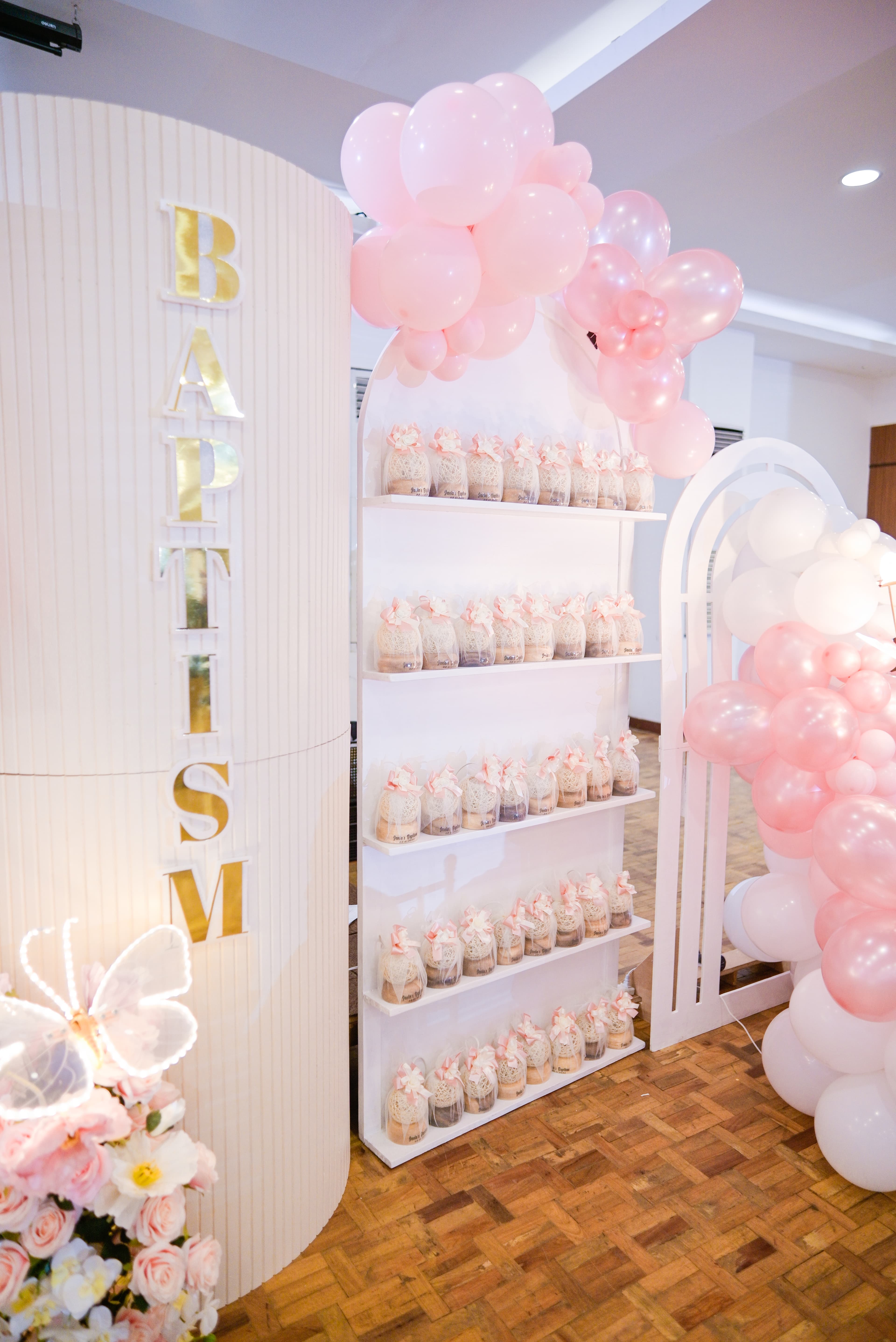 Christening favor display shelf with pink balloons and decorative arch